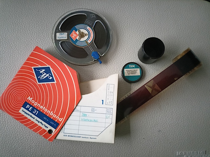 Tonband mit Schuber und Filmstreifen mit dem original Filmdöschen (r.)  auf dem Deckel des Grundig TK47 Tonbandgeräts. Hiermit wurde das Band abgespielt.